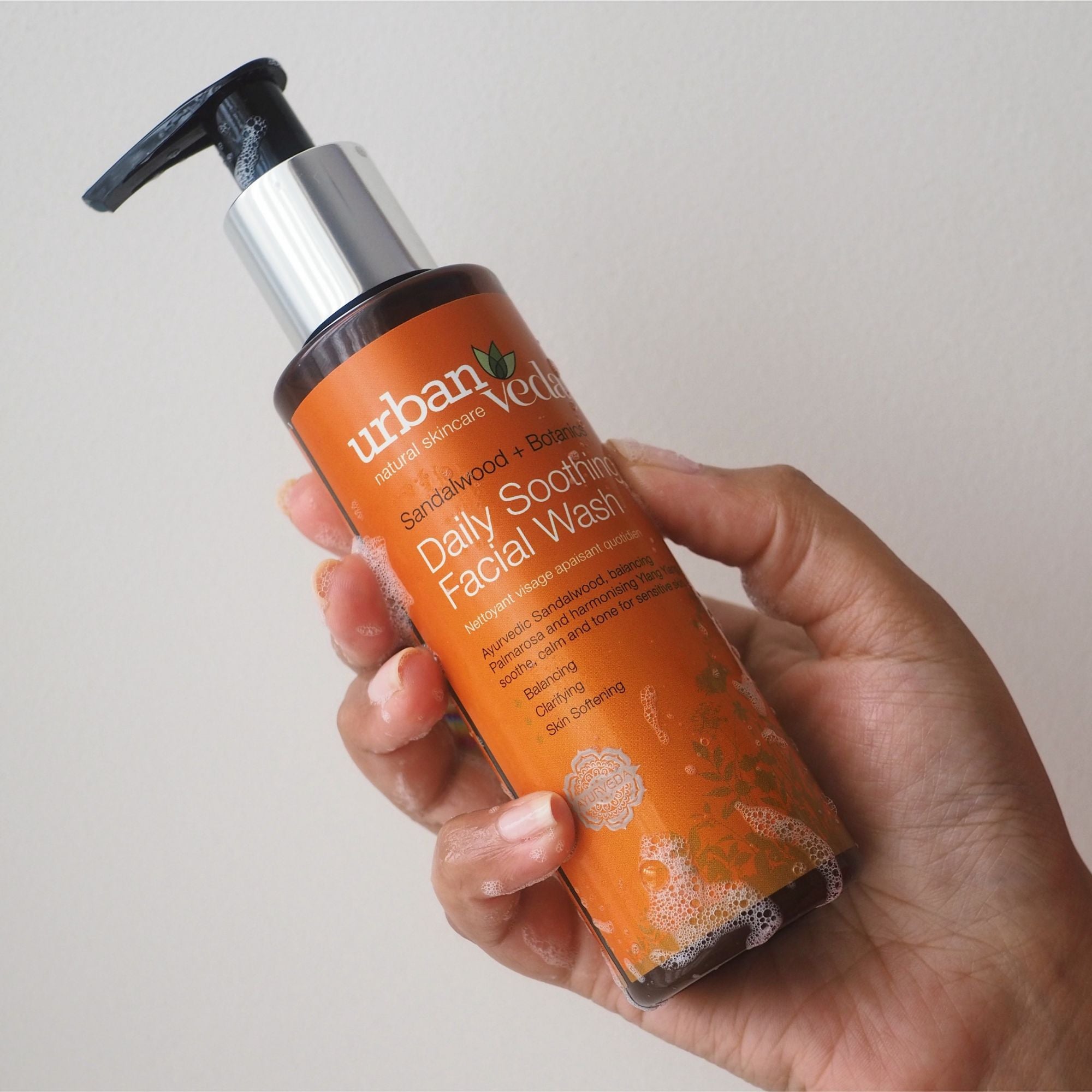 Hand holding an Urban Veda facial wash bottle against a neutral background