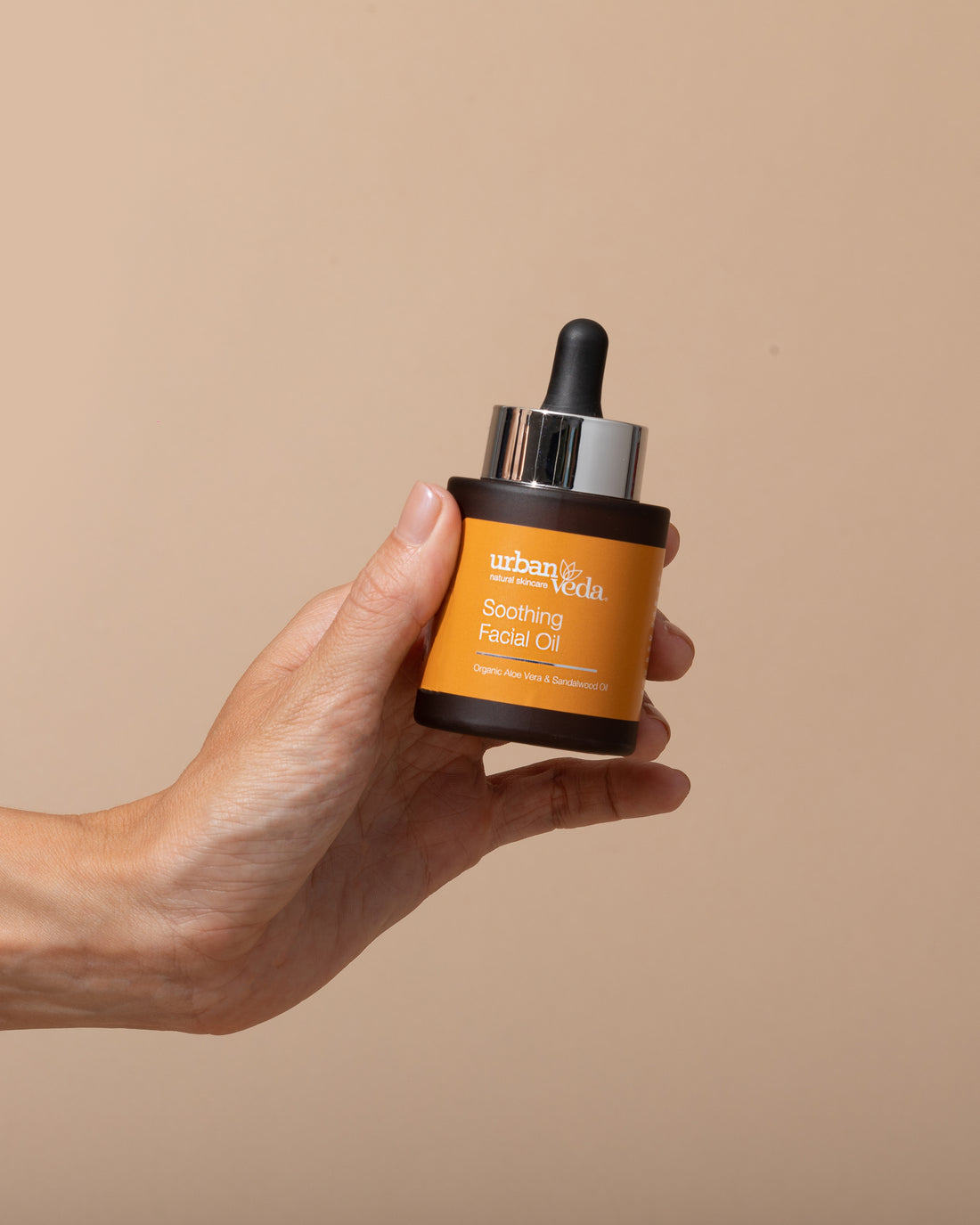Hand holding a bottle of Urban Veda Soothing Facial Oil
